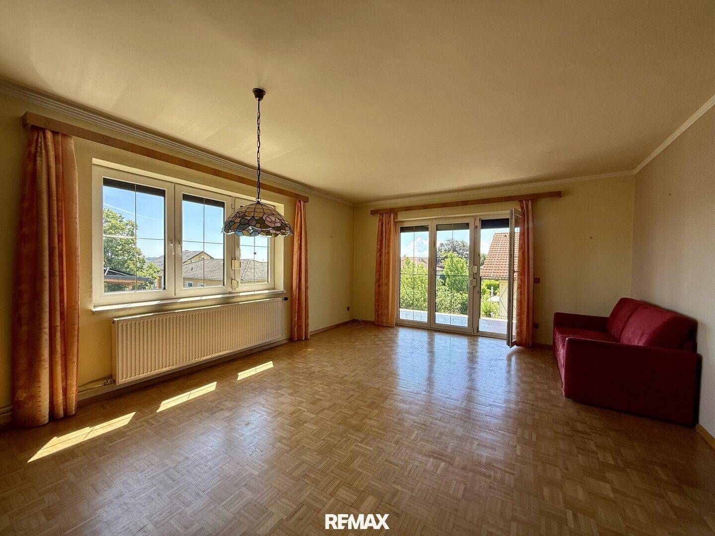 Helles Wohnzimmer mit Parkettboden, großen Fenstern und Zugang zu einem Balkon.