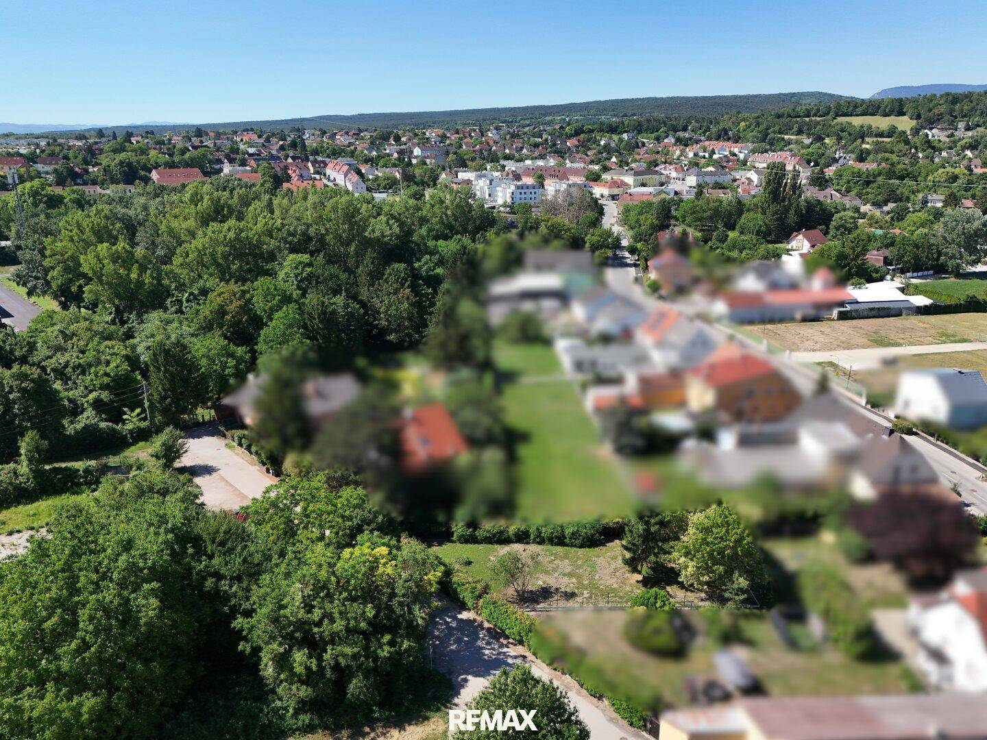 Luftaufnahme eines grünen Grundstücks, umgeben von Bäumen und Wohnhäusern, mit weitem Blick in die Ferne.