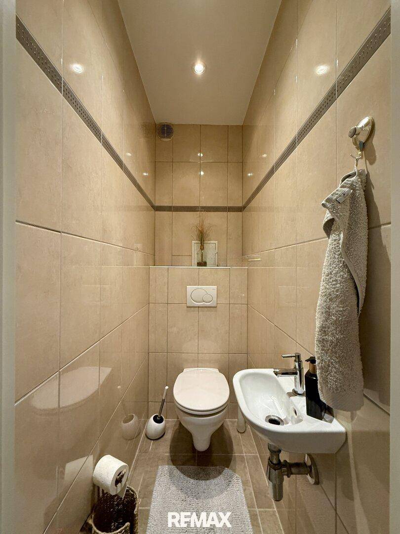 Kleines Gäste-WC mit Wand-WC, Handwaschbecken und hellen Fliesen an den Wänden.