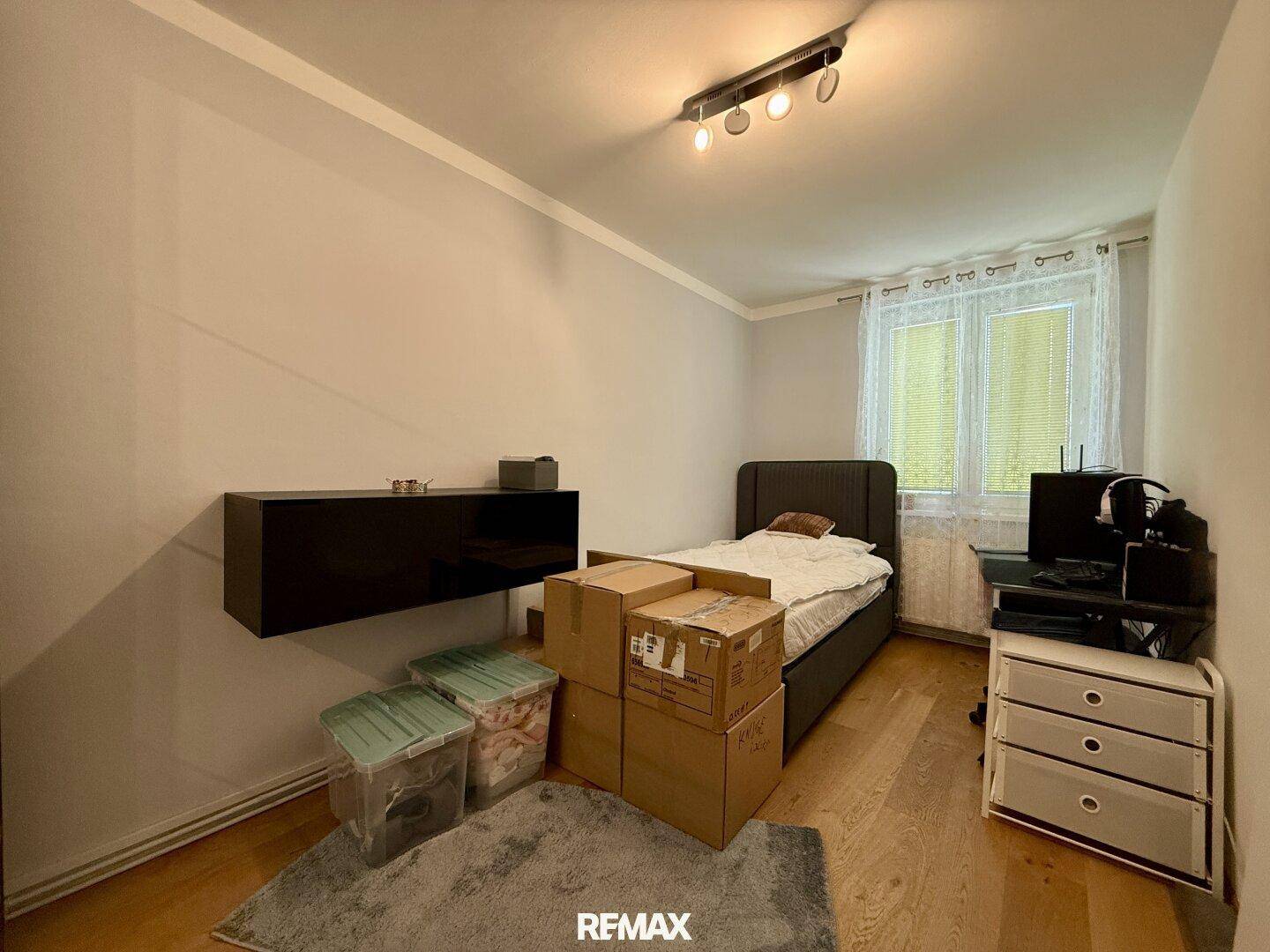 Helles Zimmer mit Einzelbett, Holzboden und einem Fenster mit Vorhängen.