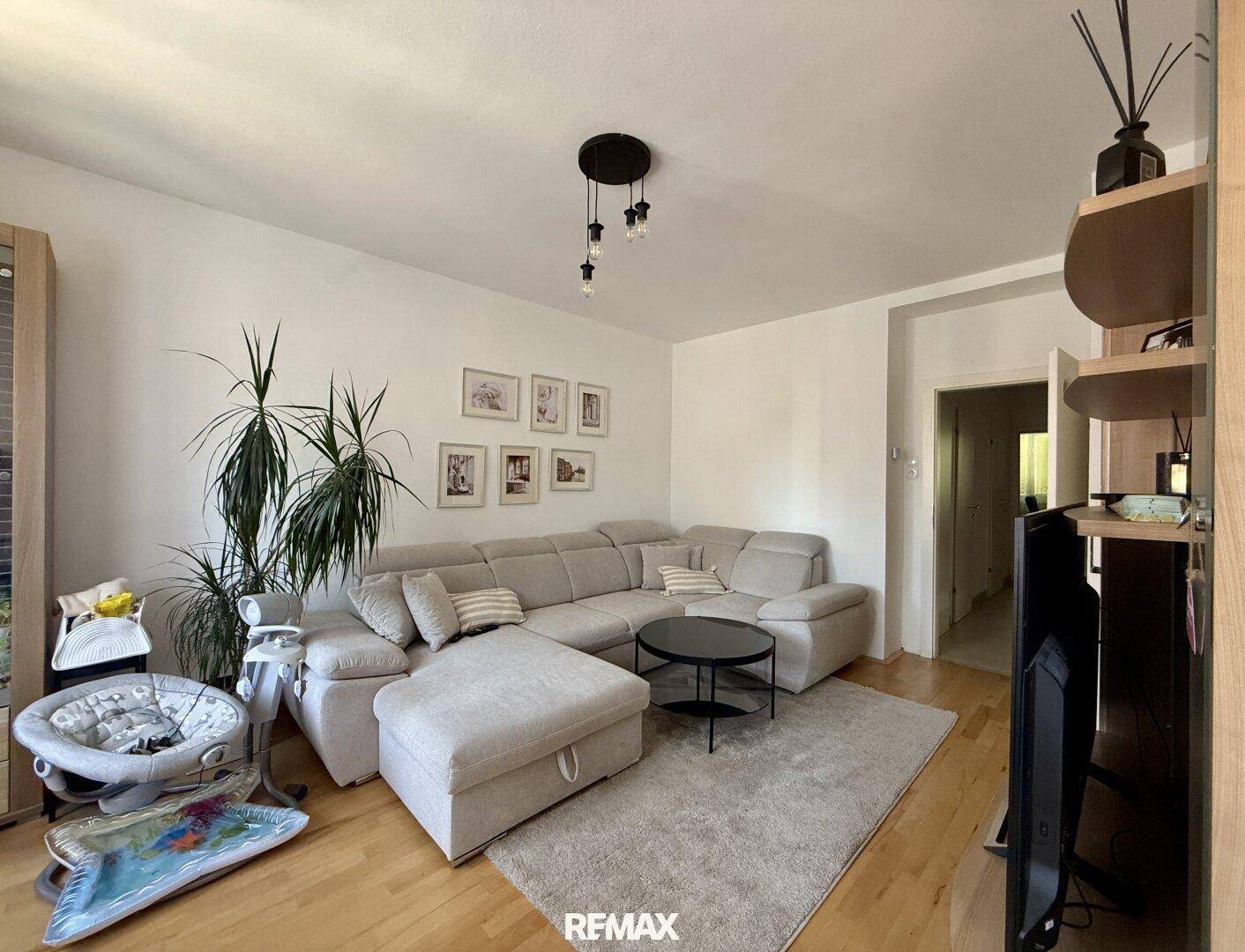 Geräumiges Wohnzimmer mit beigem Ecksofa, Holzboden und dekorativer Zimmerpflanze.