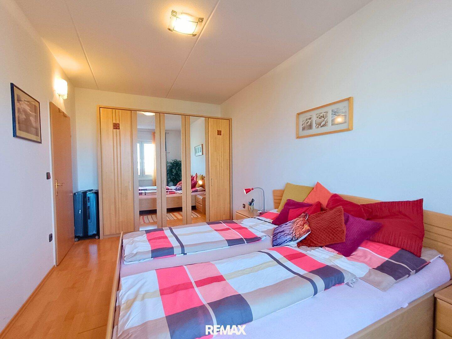 Schlafzimmer mit Holzbett und großem Spiegelschrank, der den Raum optisch erweitert.