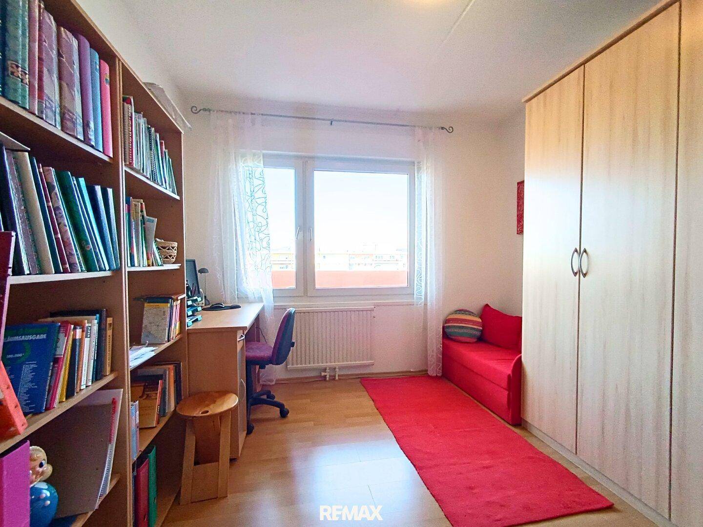Arbeitszimmer mit Bücherregal, Schreibtisch und Fenster, das viel Tageslicht hereinlässt.