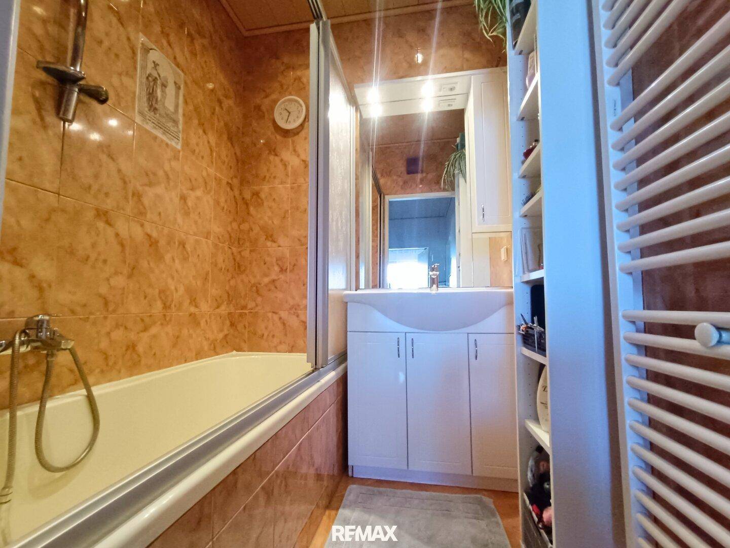 Badezimmer mit Badewanne, braunen Fliesen und einem Waschbecken mit Spiegelschrank.