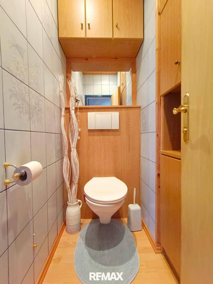 Separate Toilette mit Wand-WC, hellen Fliesen und Holzverkleidung.