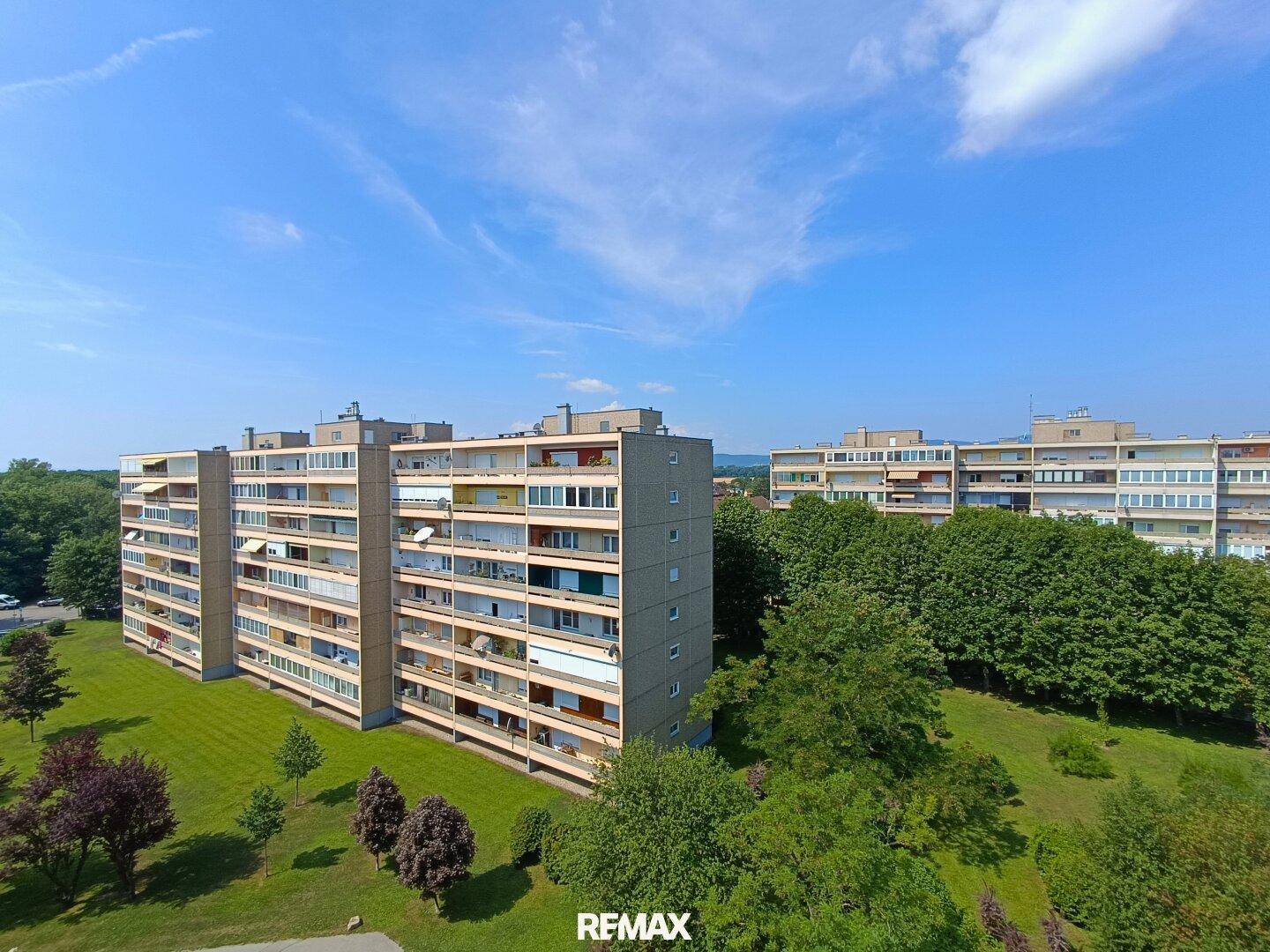 Mehrere Wohngebäude in einer grünen Umgebung unter blauem Himmel.