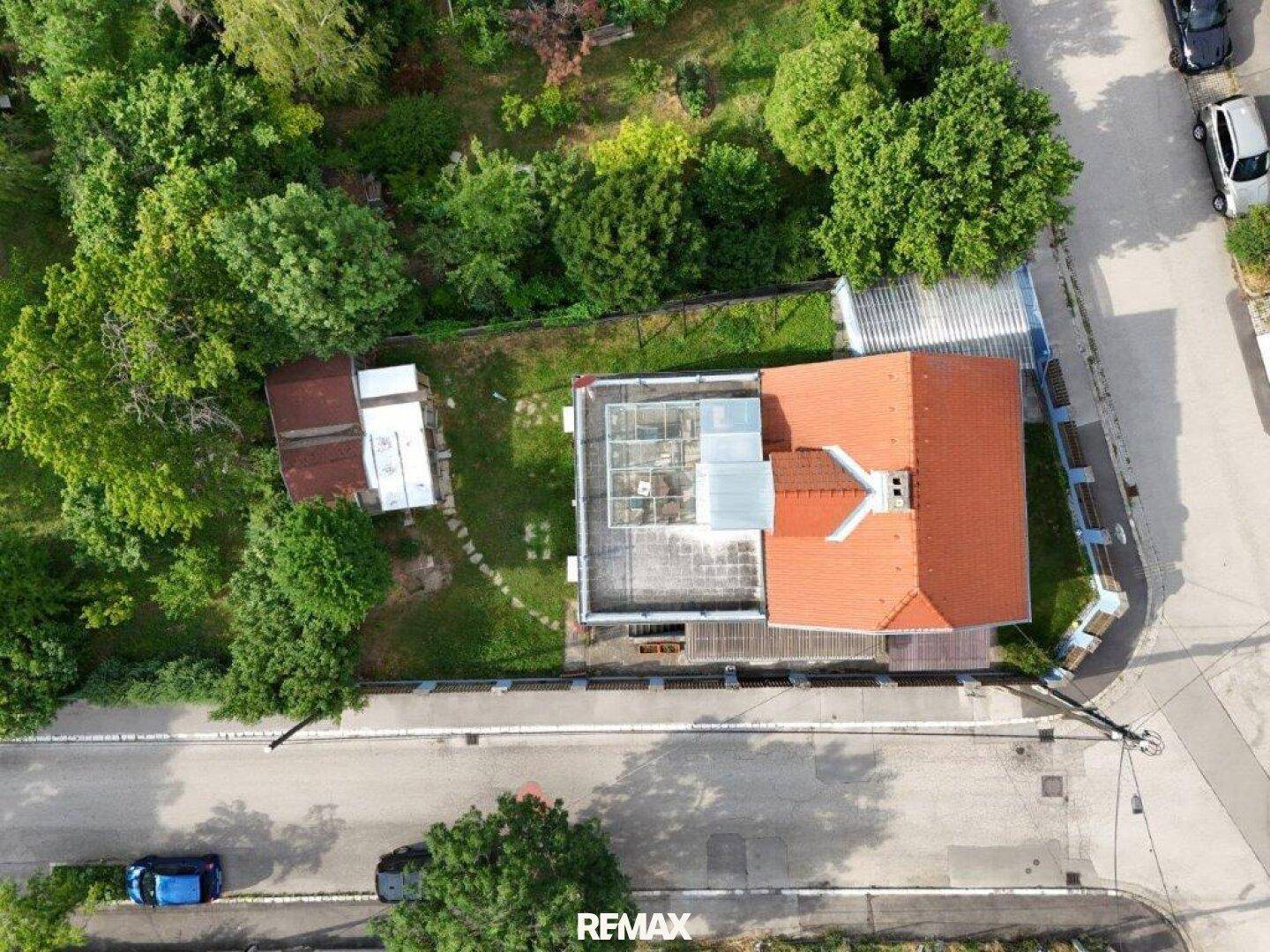 Draufsicht auf das Wohnhaus mit rotem Ziegeldach, Garten, Carport und umliegender grüner Landschaft.