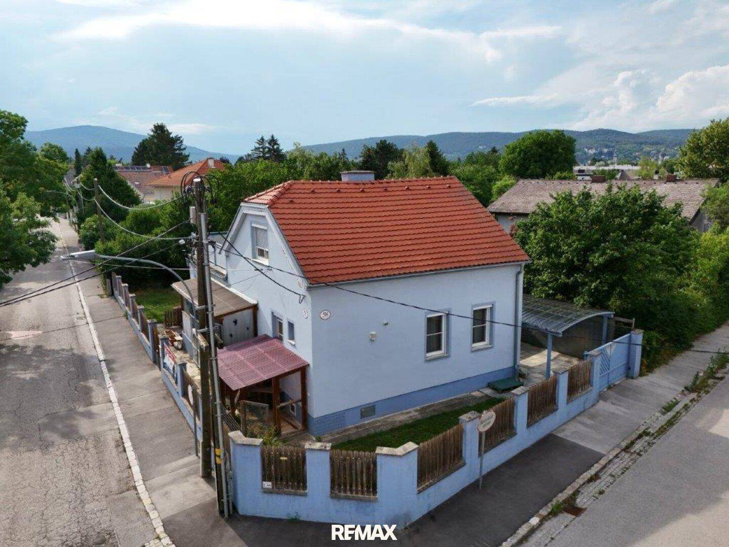 Seitenansicht des Hauses mit hellblauer Fassade, rotem Dach, Carport und Blick auf die umliegende Natur.