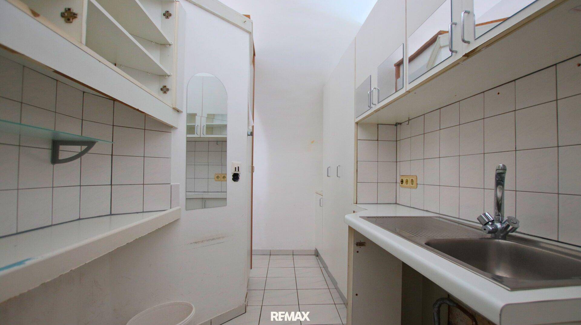 Schmaler Hauswirtschaftsraum oder kleine Küche mit Spülbecken, einfachen Schränken und gefliesten Wänden.