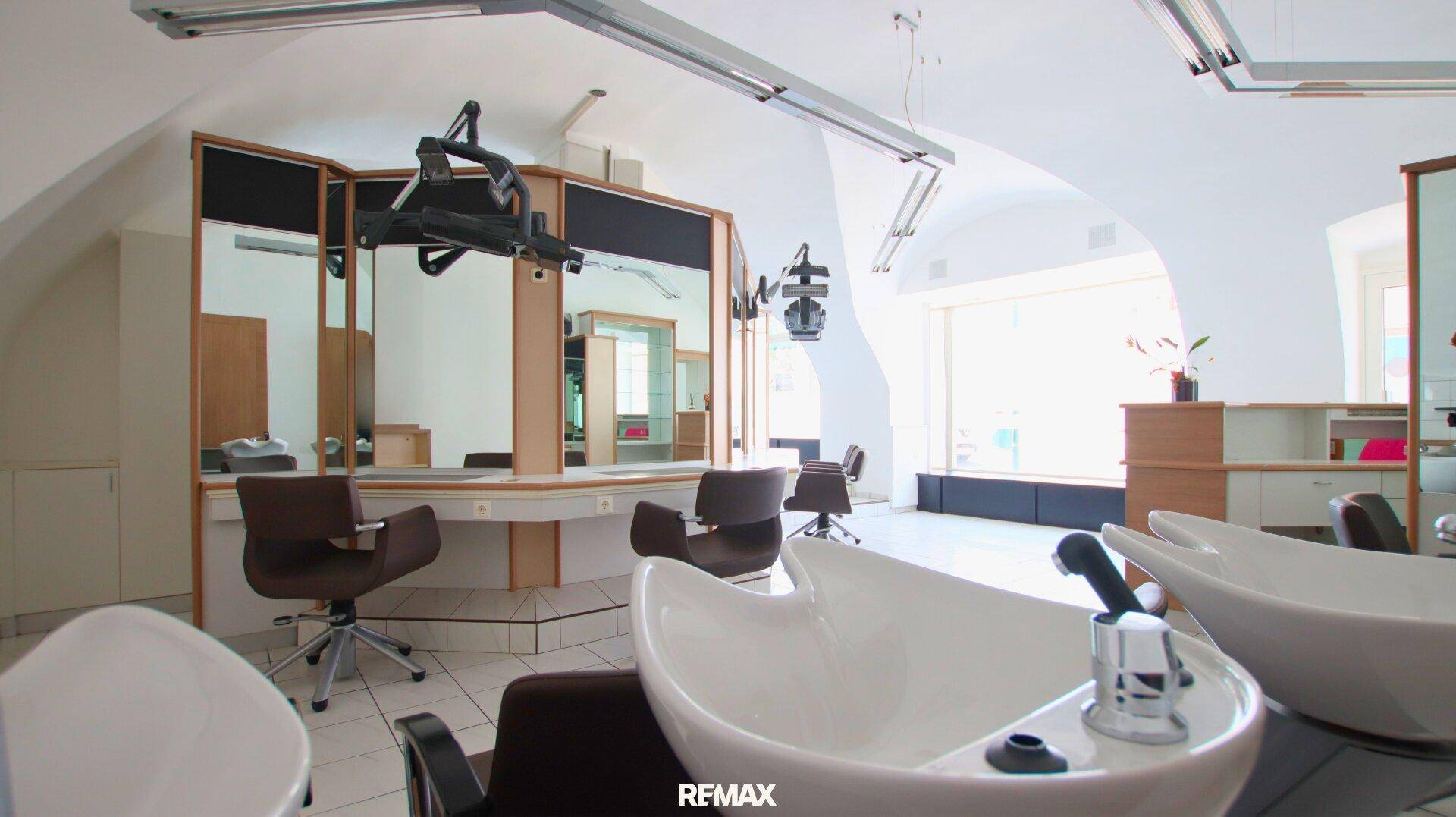 Perspektive von den Haarwaschbecken auf die Styling-Bereiche und die großen Fensterfronten des Friseursalons.
