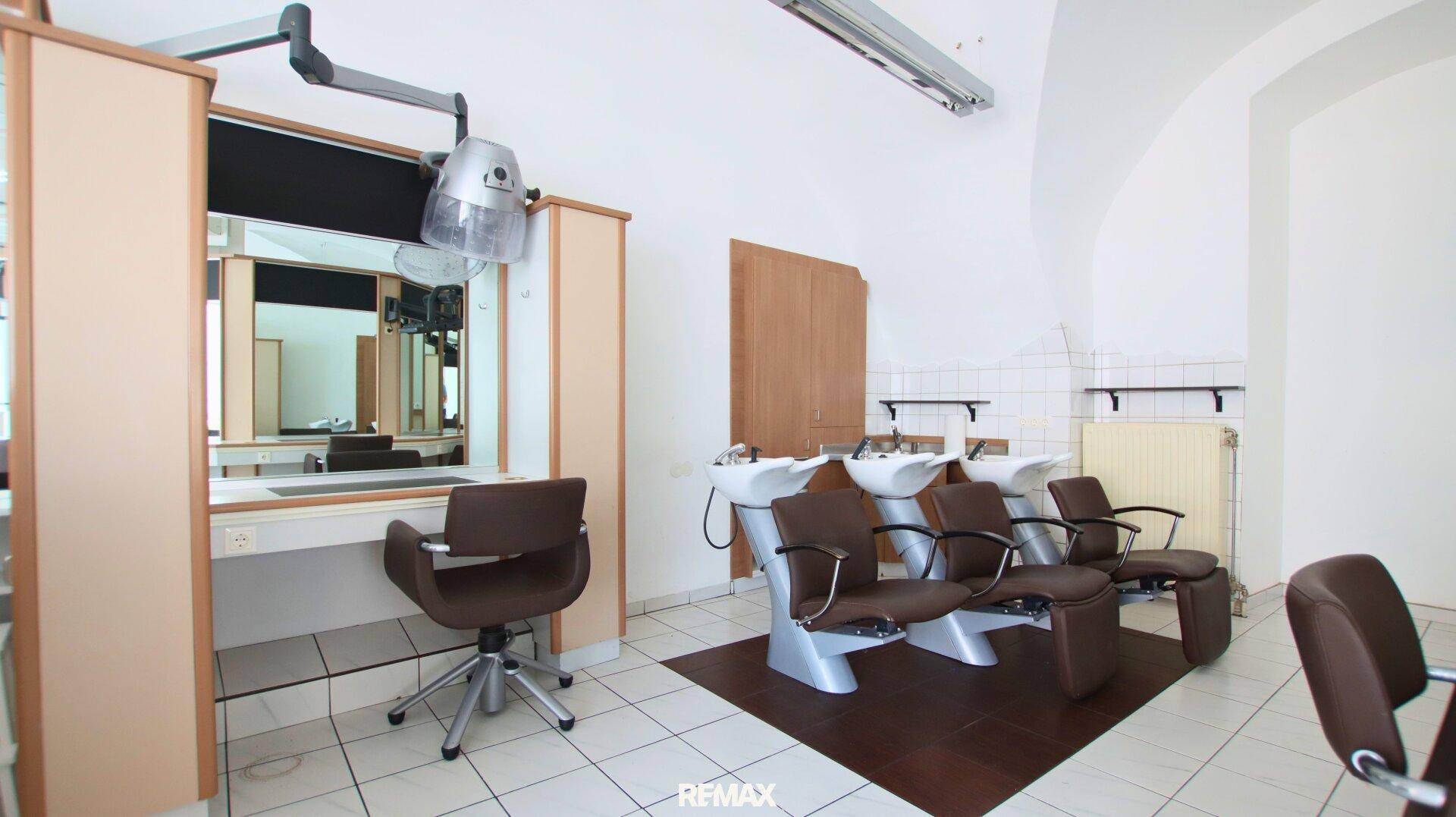 Bereich mit Haarwaschbecken und Stühlen, daneben eine Styling-Station mit Trockenhaube und Spiegel.