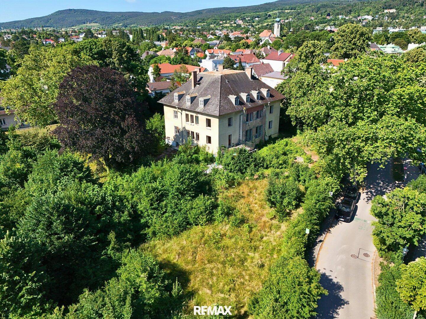 Luftaufnahme eines großen, älteren Hauses mit weitläufigem, bewachsenem Grundstück in einer grünen Umgebung.