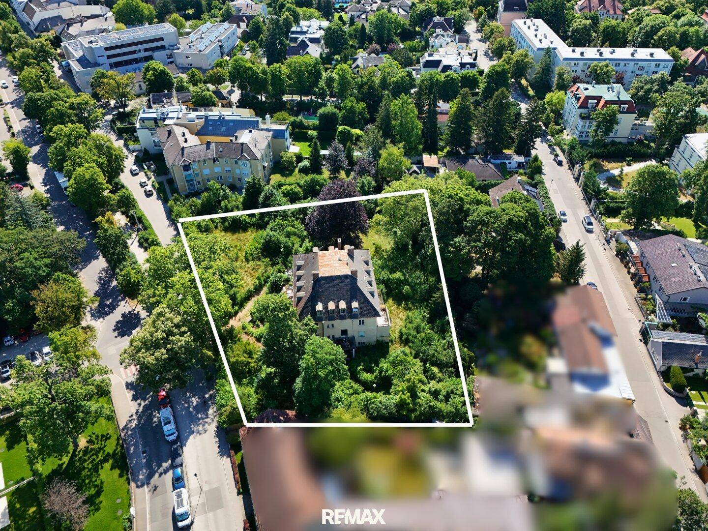 Luftaufnahme eines Anwesens mit markierten Grundstücksgrenzen, umgeben von viel Grün und weiteren Gebäuden.