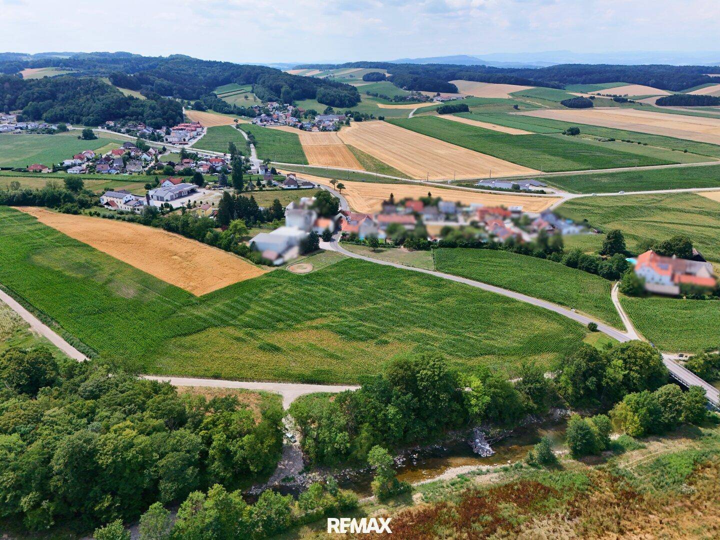 Panoramablick aus der Luft auf eine ländliche Umgebung mit Ackerland, Wäldern und einem kleinen Dorf am Horizont.