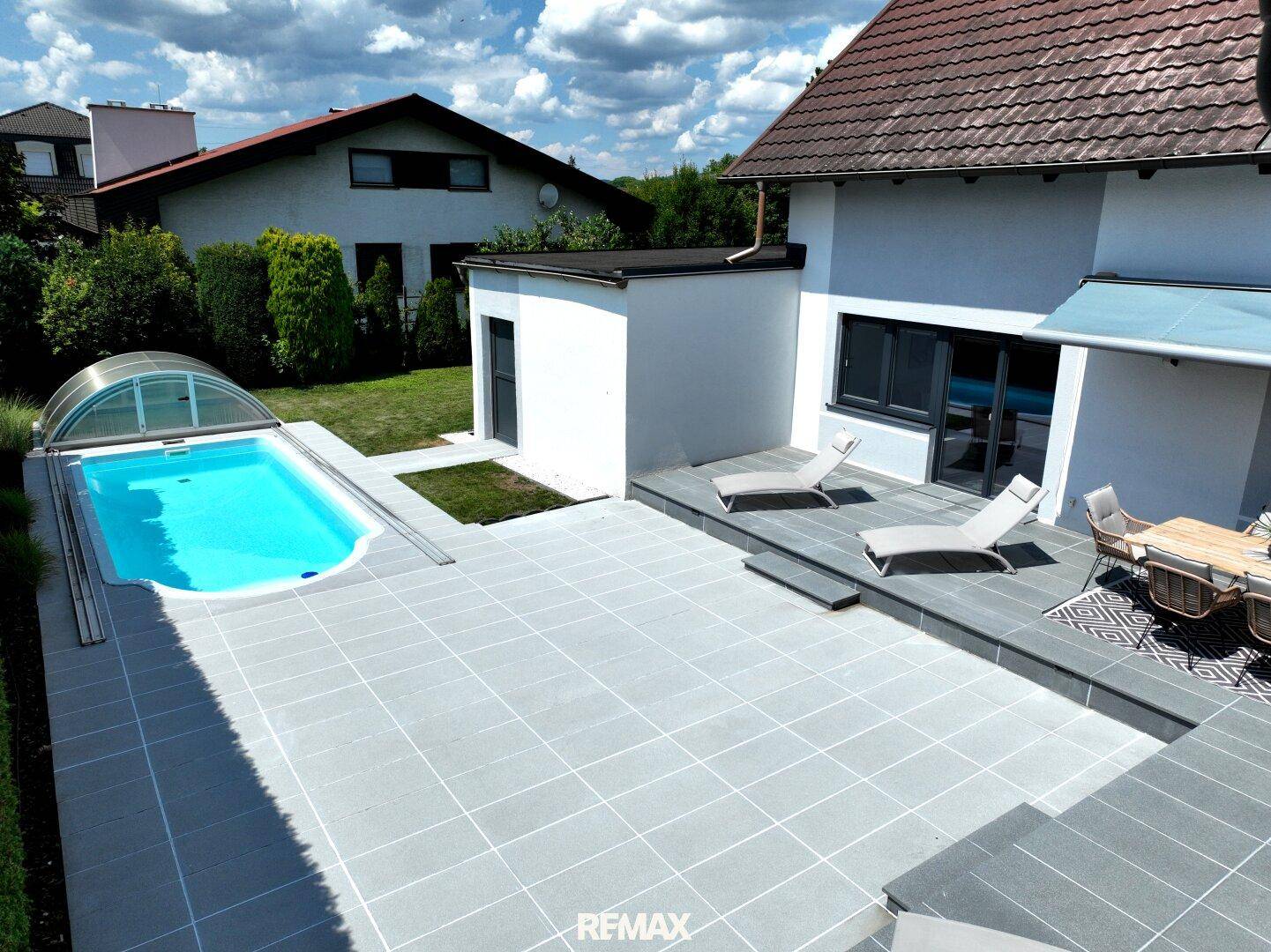 Weitläufige Terrasse mit Pool und Sonnenliegen, umgeben von Grünflächen.