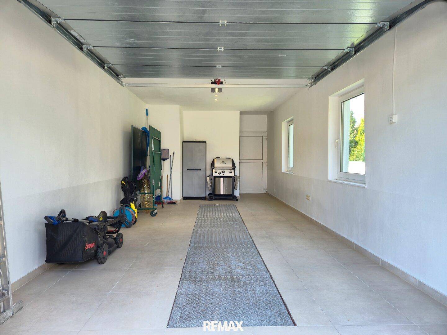 Geräumige Garage mit Fliesenboden, Fenstern und Stauraum.