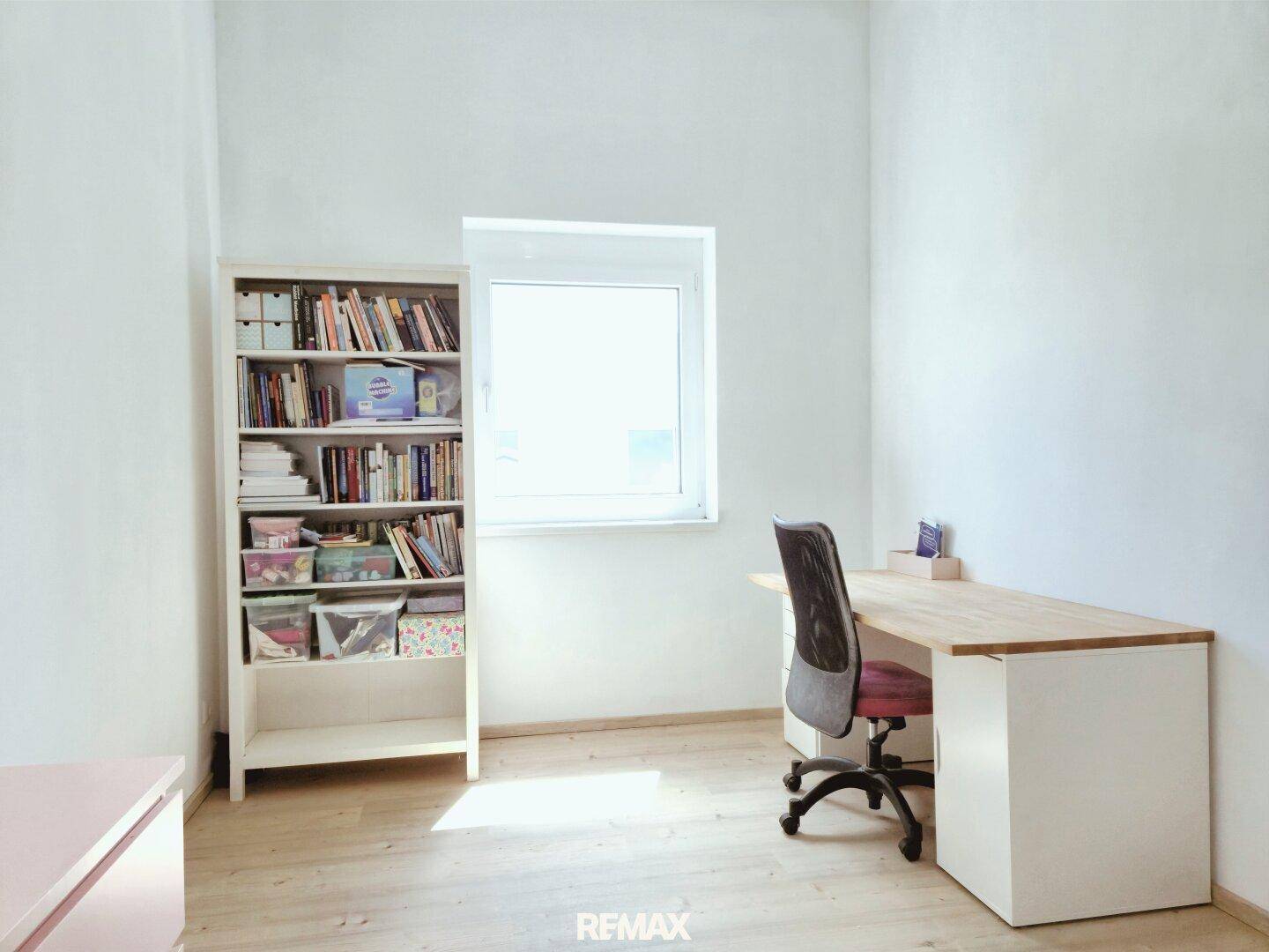 Ruhiges Arbeitszimmer mit Schreibtisch, Bücherregal und viel Tageslicht.