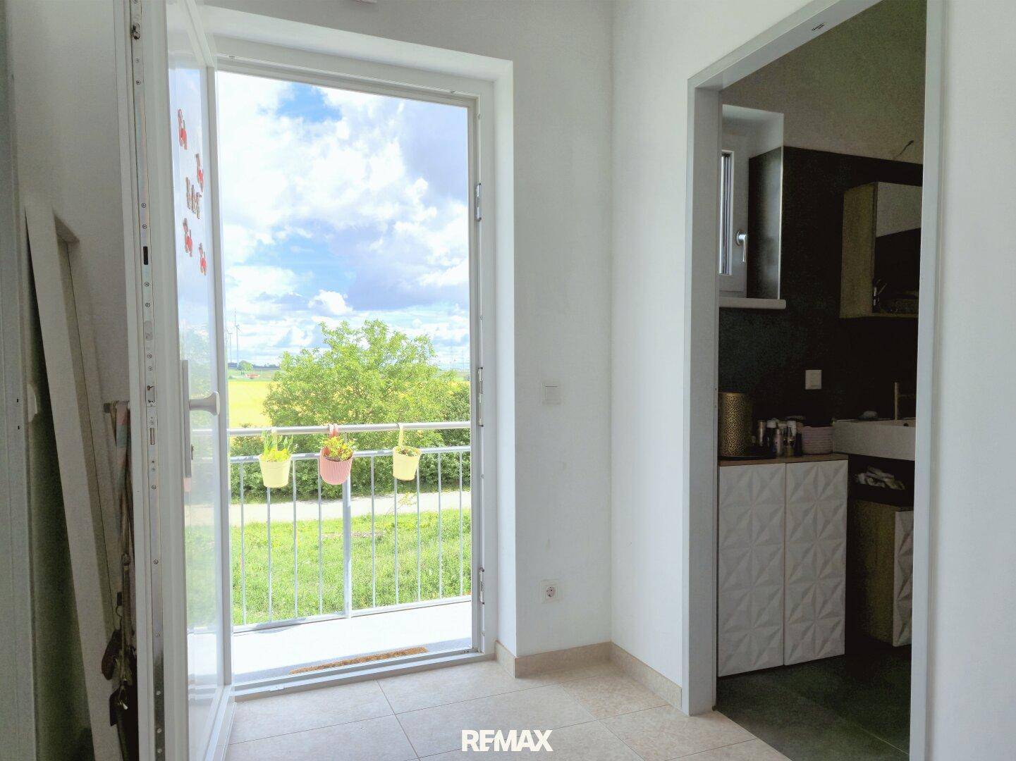Heller Flur mit Zugang zu einem kleinen Balkon und Blick ins Grüne.