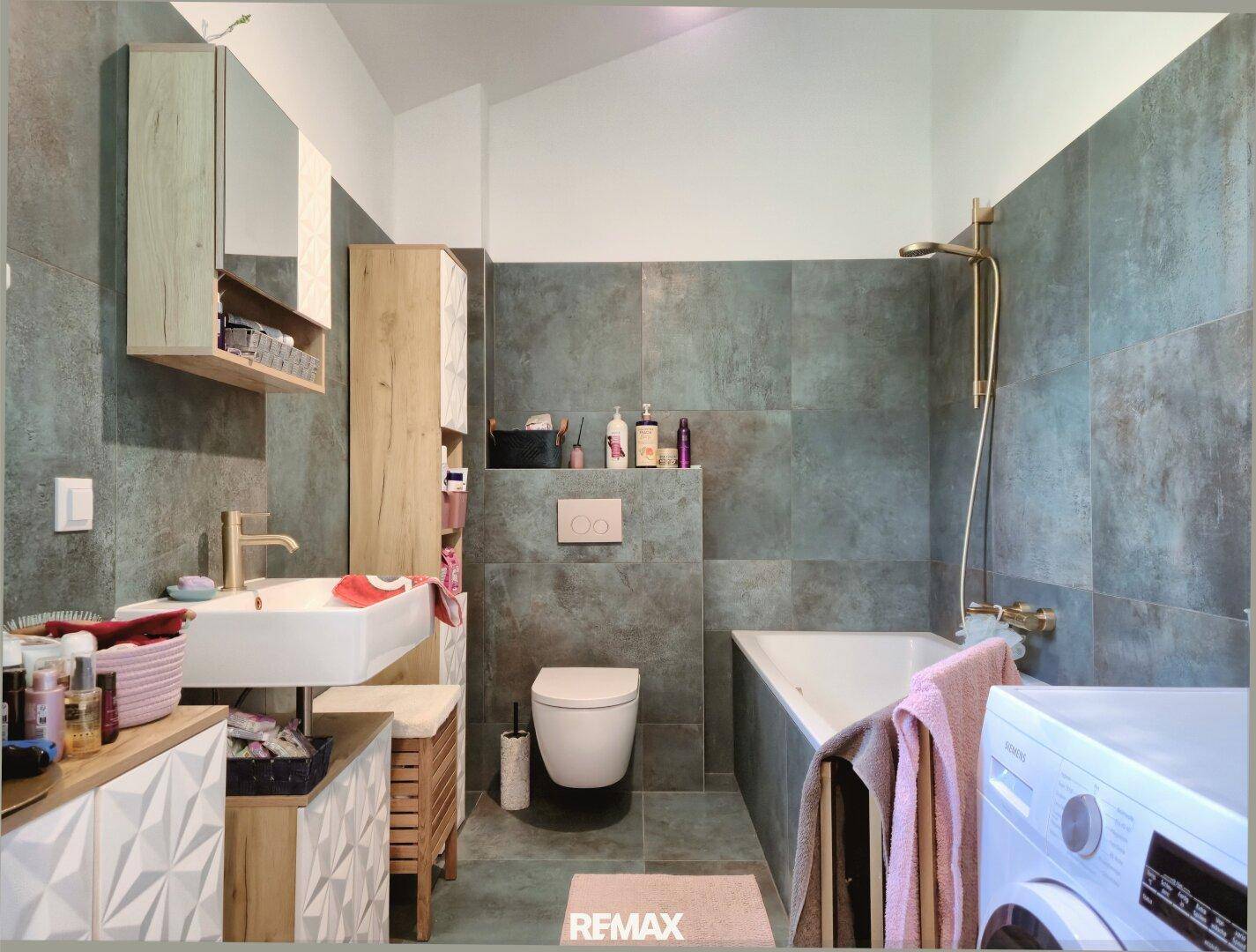 Modernes Badezimmer mit dunklen Fliesen, Badewanne, Dusche und Waschmaschine.