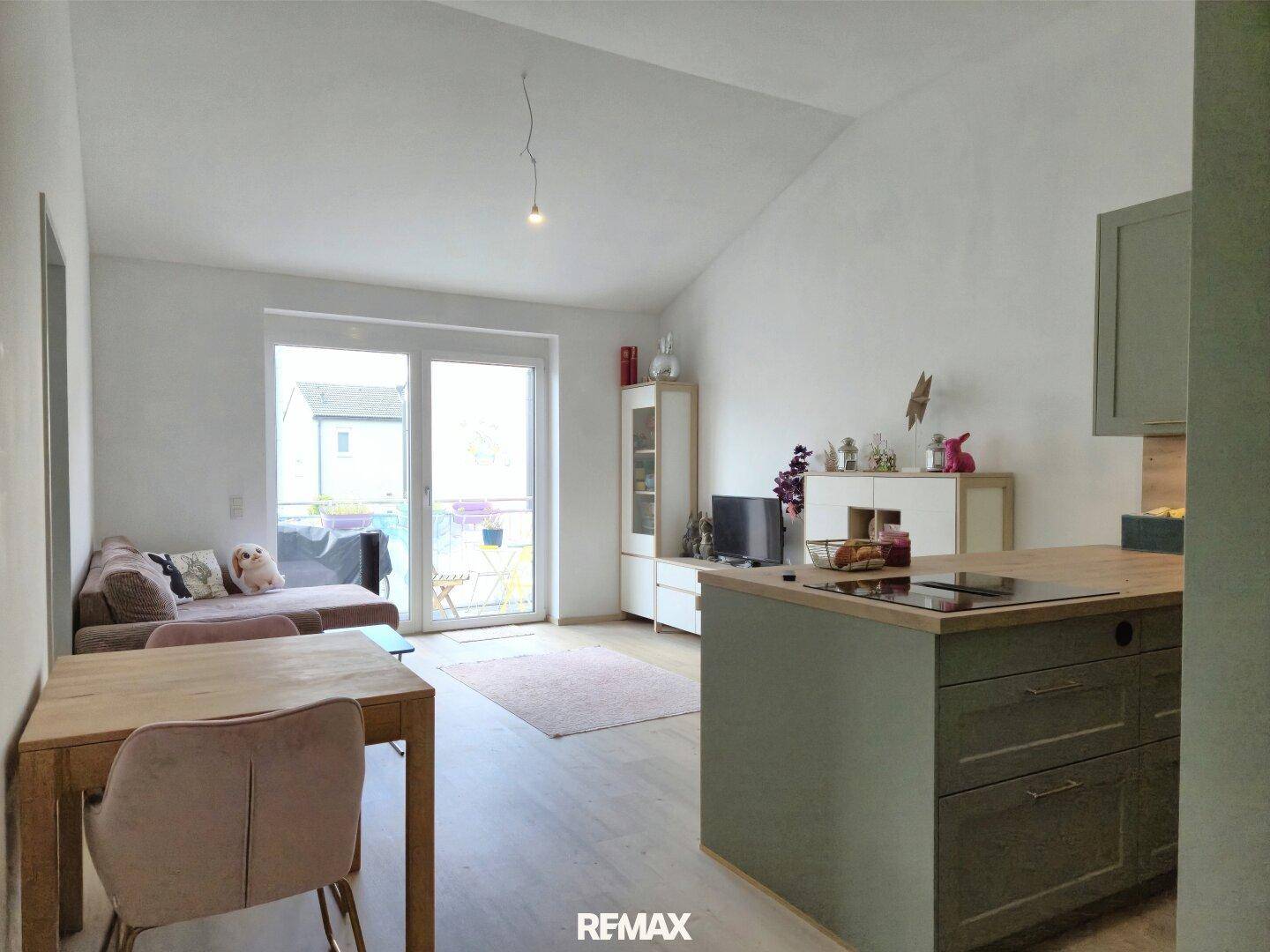 Offener Wohnbereich mit Essplatz, Küche und Zugang zu einem Balkon.