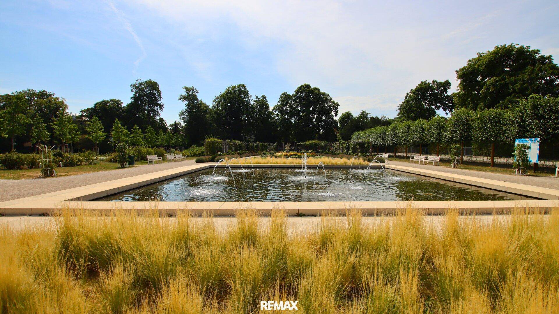 Formaler Garten mit rechteckigem Wasserbecken und Springbrunnen, umgeben von gepflegten Grünflächen.