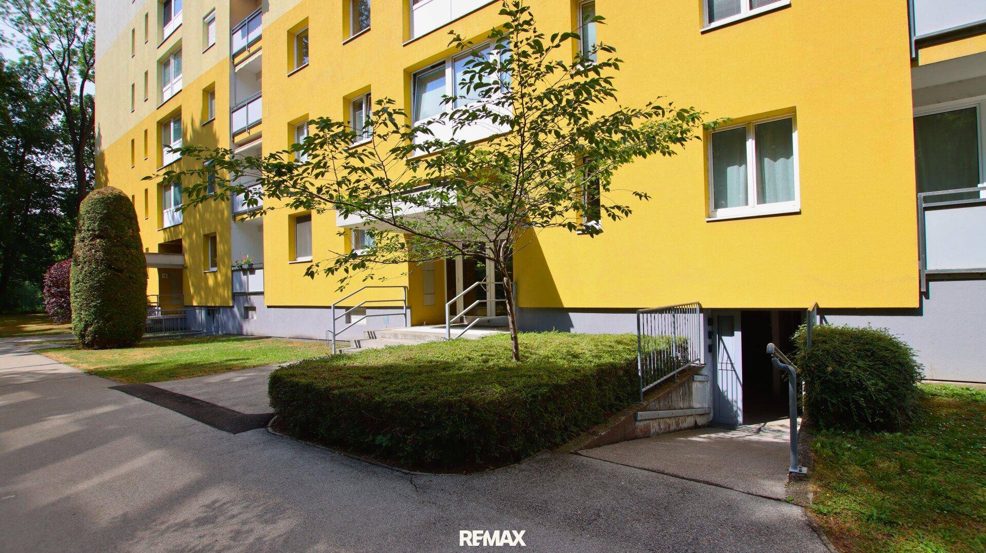 Gelbes Mehrfamilienhaus mit Eingangsbereich, Treppen und gepflegten Grünflächen.