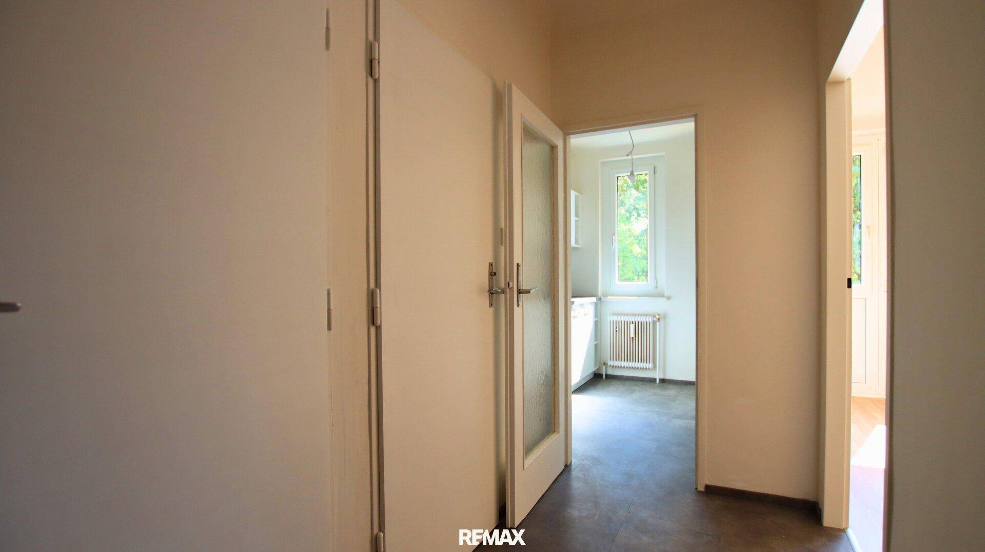 Heller Flur mit mehreren Türen, eine davon führt in einen Raum mit Fenster.