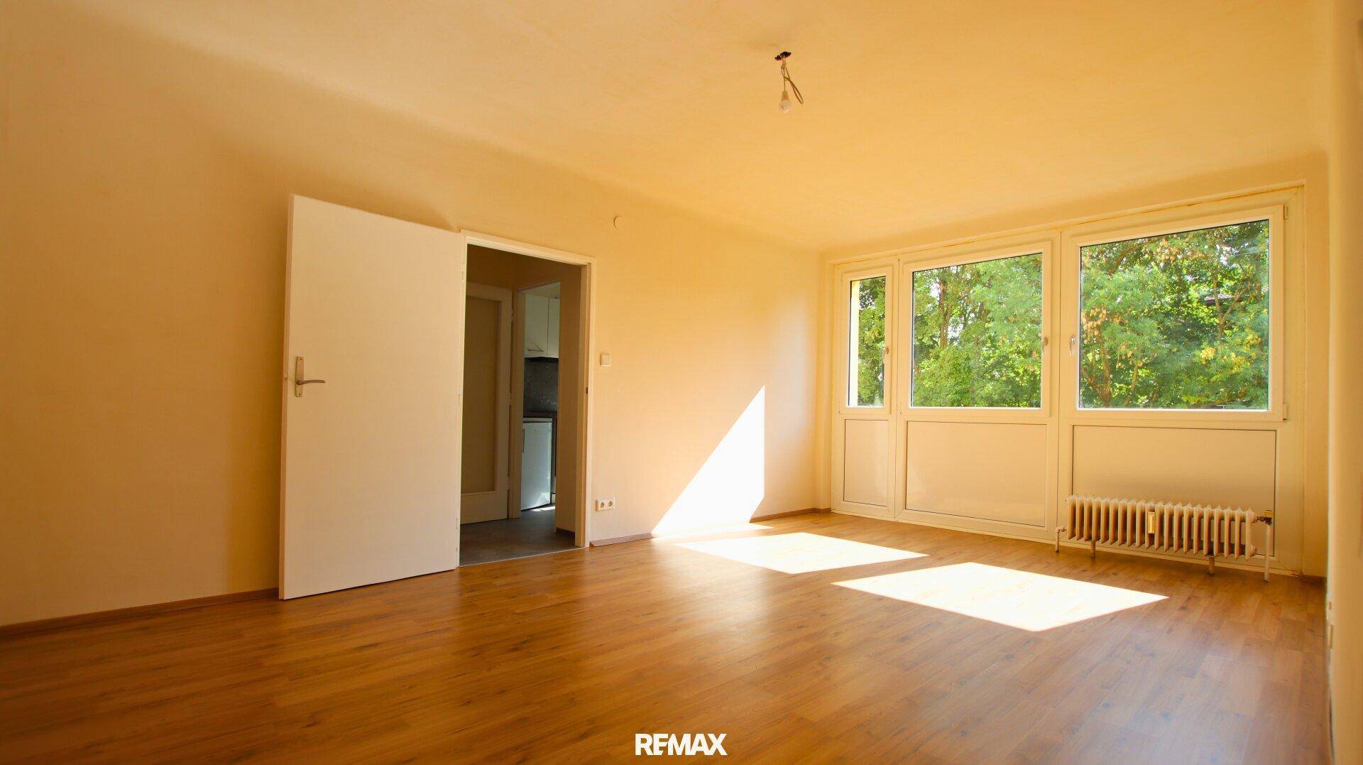Geräumiges Wohnzimmer mit Holzboden, großen Fenstern und viel natürlichem Sonnenlicht.