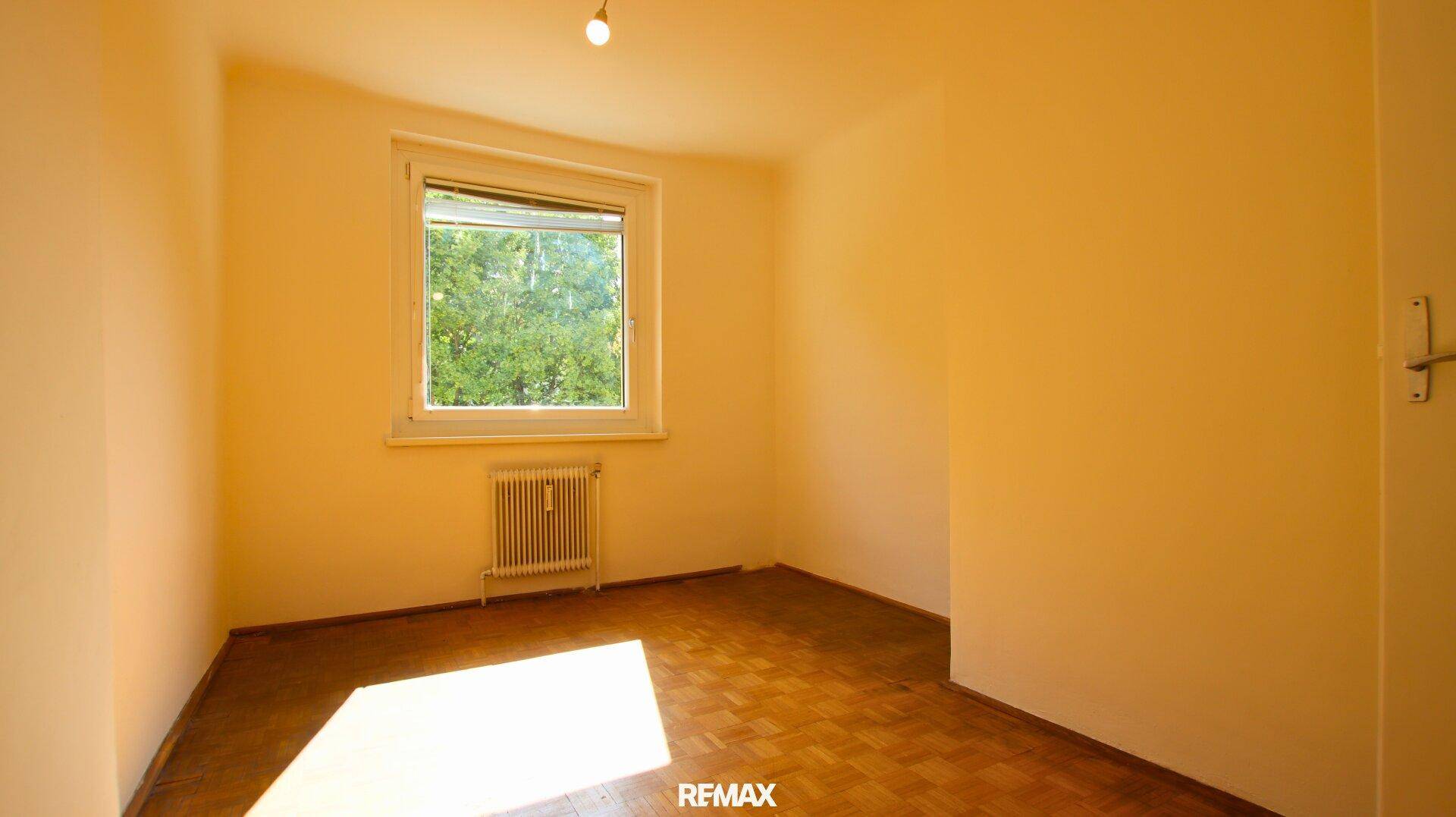 Helles Schlafzimmer mit Parkettboden, Fenster und Blick ins Grüne.