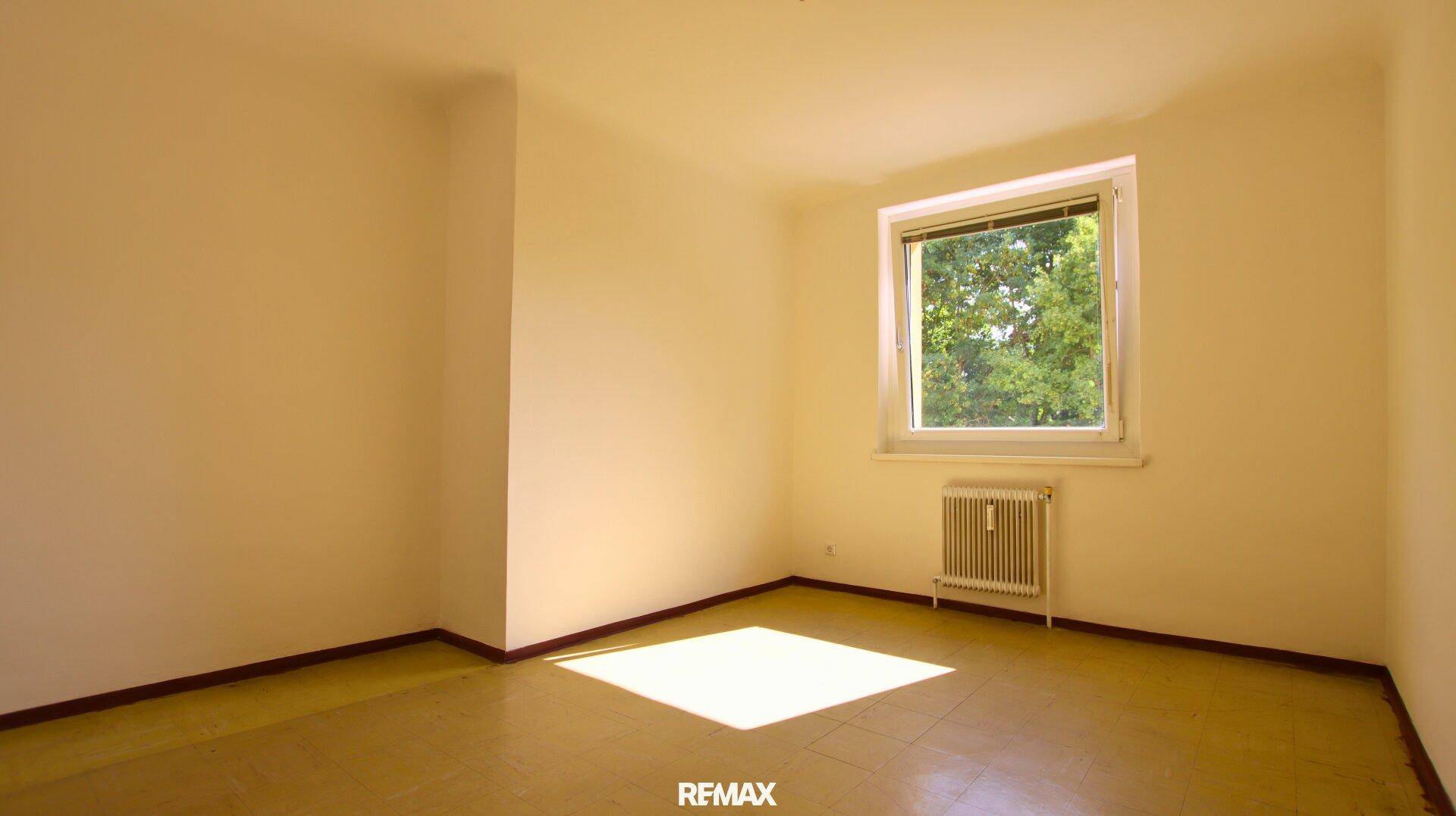 Geräumiges Schlafzimmer mit Parkettboden, Fenster und Blick ins Grüne.