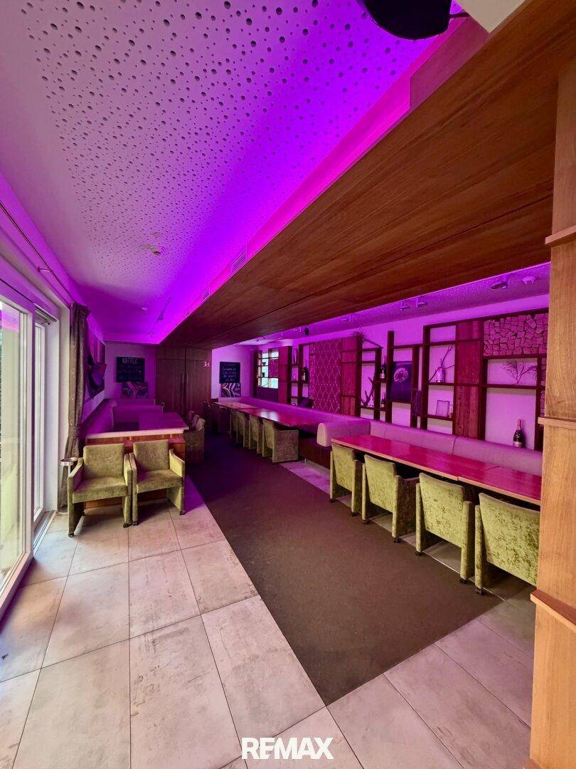 Langer Restaurantbereich mit Reihen von Tischen und Stühlen, beleuchtet von stimmungsvollem violettem Licht.