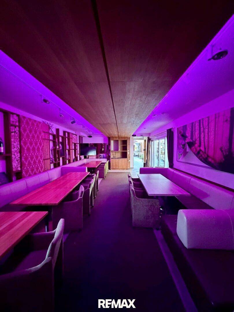 Weitläufiger Gastraum mit langen Sitzbänken und Tischen, akzentuiert durch moderne violette Beleuchtung.