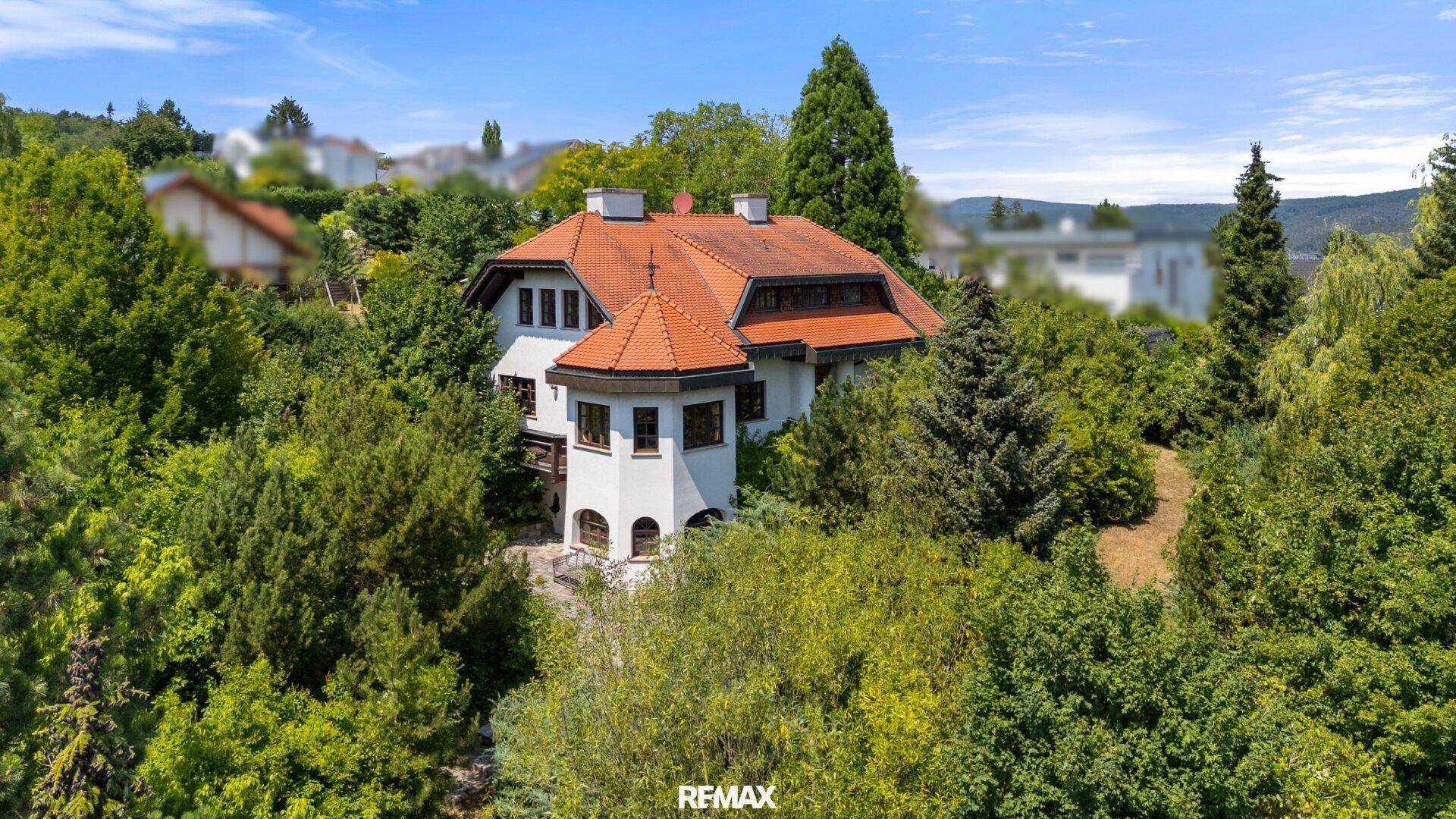 Traditionelles Haus mit rotem Ziegeldach, umgeben von üppigem Grün und Bäumen in einer ruhigen Umgebung.