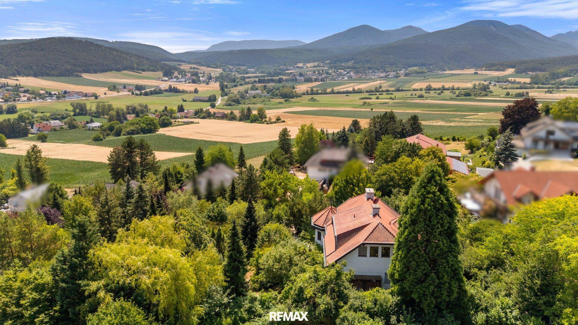 Malerische Landschaft mit grünen Hügeln, Feldern und einem charmanten Haus in der Ferne.