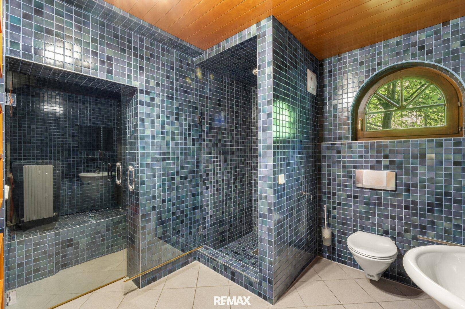 Einzigartiges Badezimmer mit blauen Mosaikfliesen, großer Dusche und Rundbogenfenster.