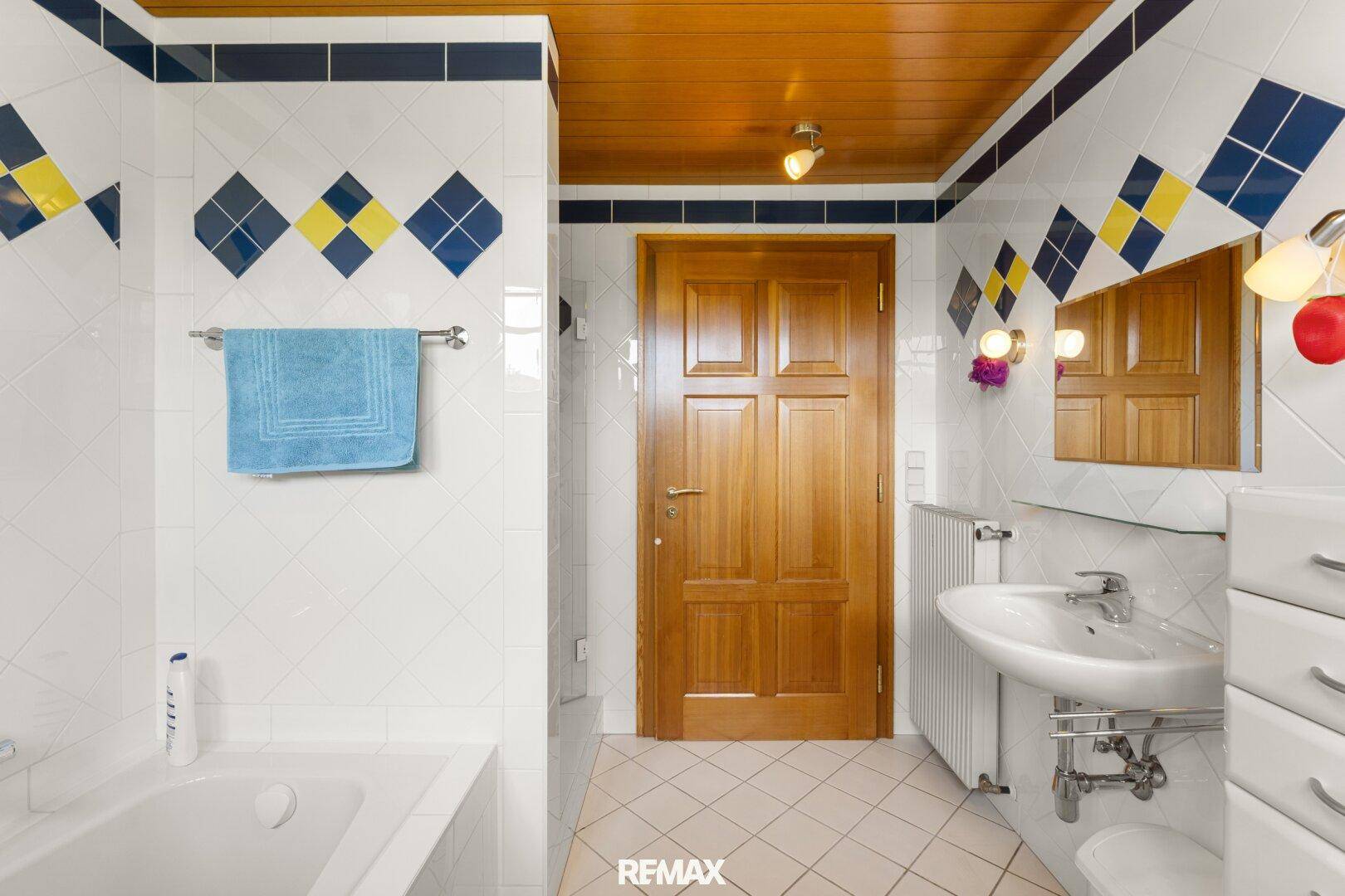 Badezimmer mit Badewanne, Fliesen in Blau-Gelb-Muster und Holzdecke.
