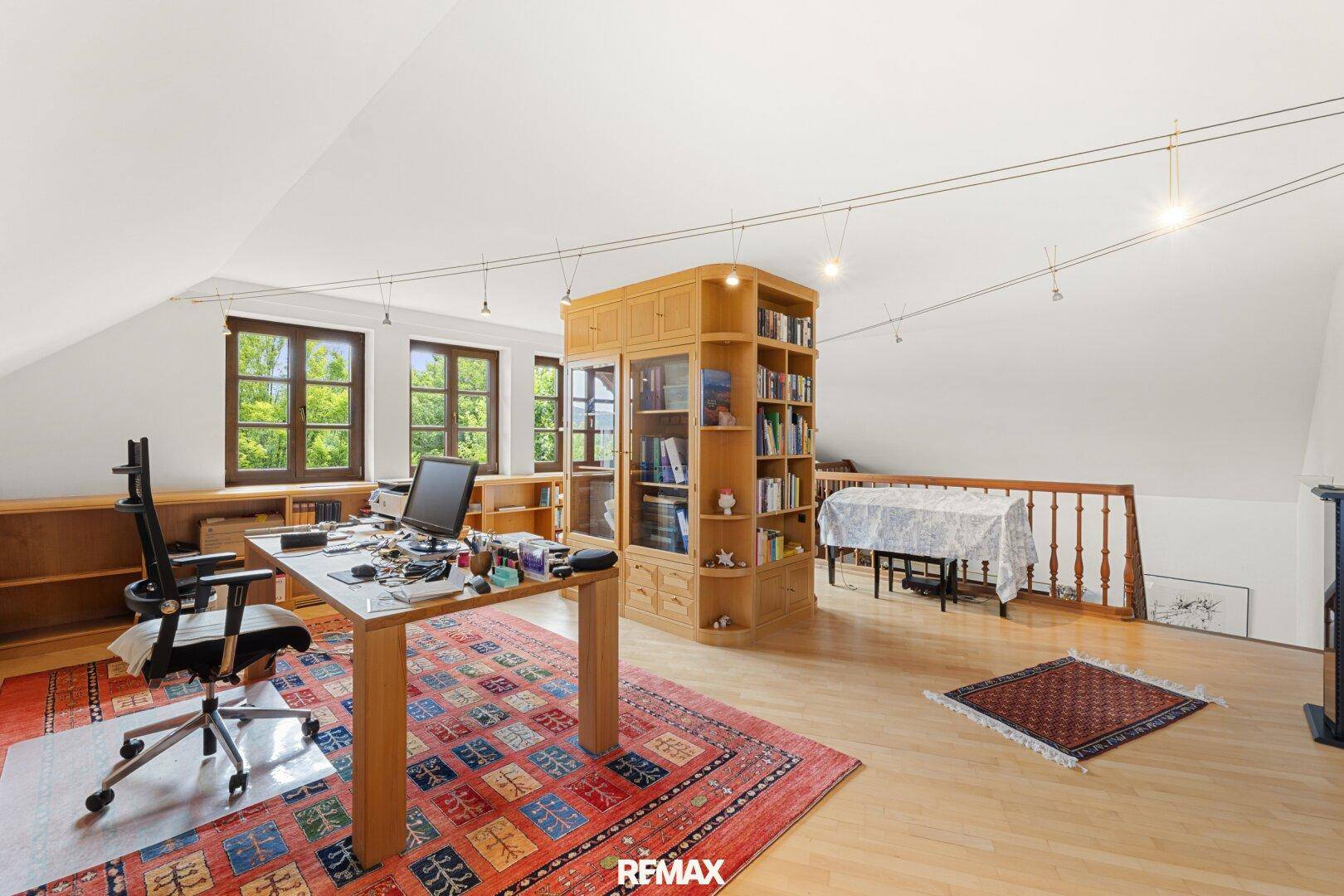 Helles Dachgeschoss-Büro mit Holzboden, Einbauregalen und Blick ins Grüne.