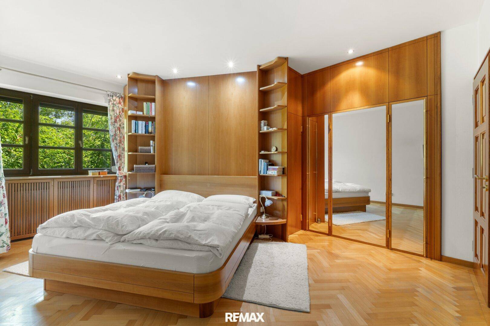 Geräumiges Schlafzimmer mit Holzboden, Einbauschränken und Blick ins Grüne.