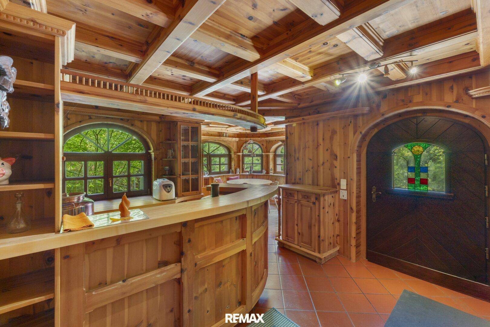 Rustikale Holzküche mit Bar, Rundbogenfenstern und Zugang zu einem weiteren Raum.
