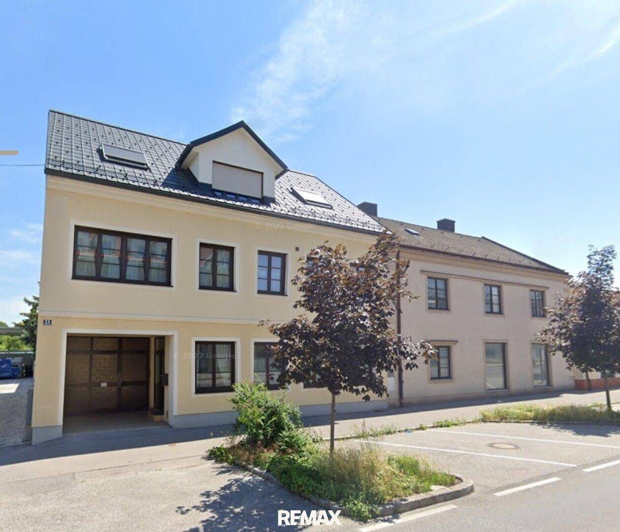 Ansicht der Gebäudefassade von der Straße mit Parkplätzen und Bäumen im Vordergrund.