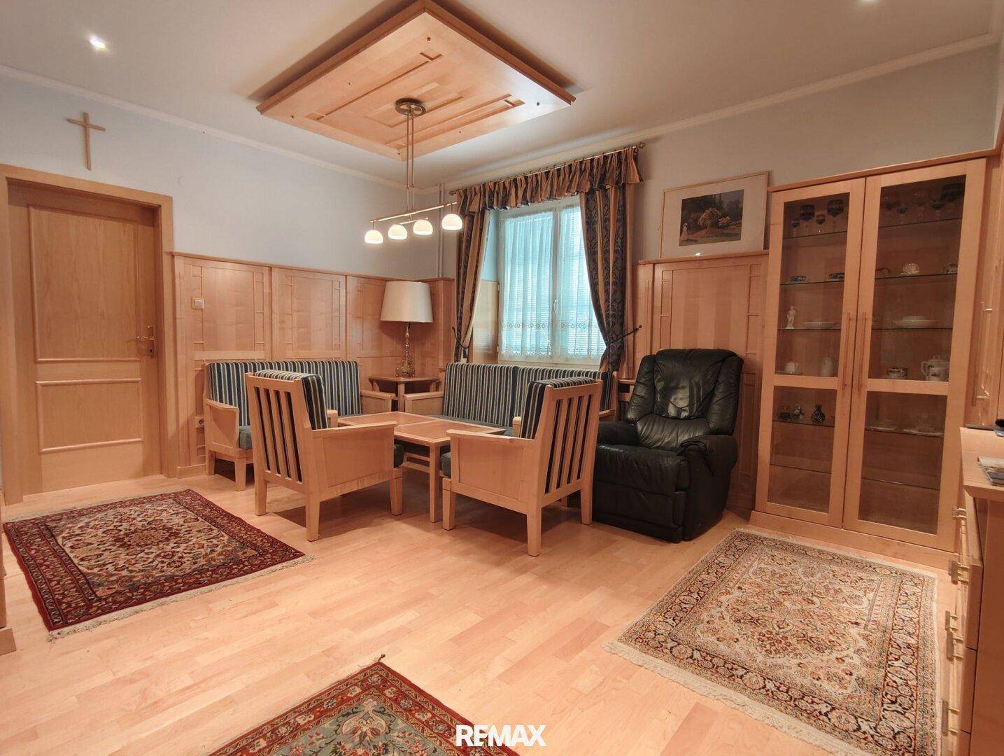 Geräumiges Wohnzimmer mit Holzvertäfelung, Parkettboden und bequemen Sitzgelegenheiten.
