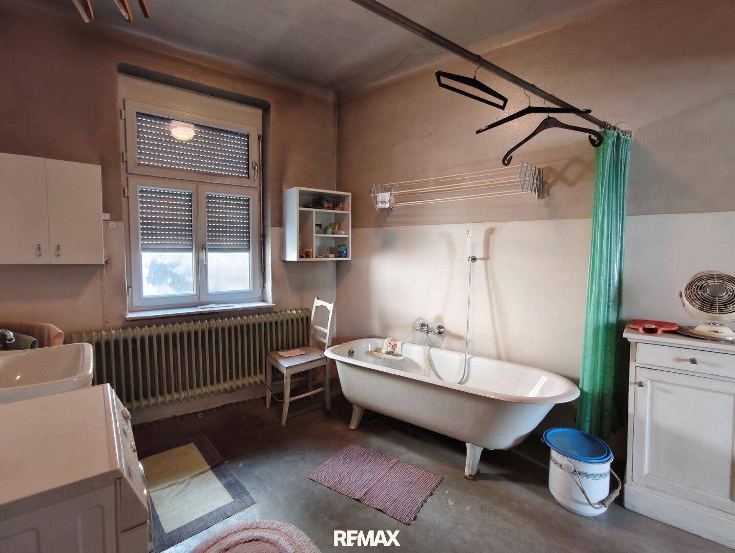 Geräumiges Badezimmer mit freistehender Badewanne, Waschbecken und Fenster, renovierungsbedürftig.