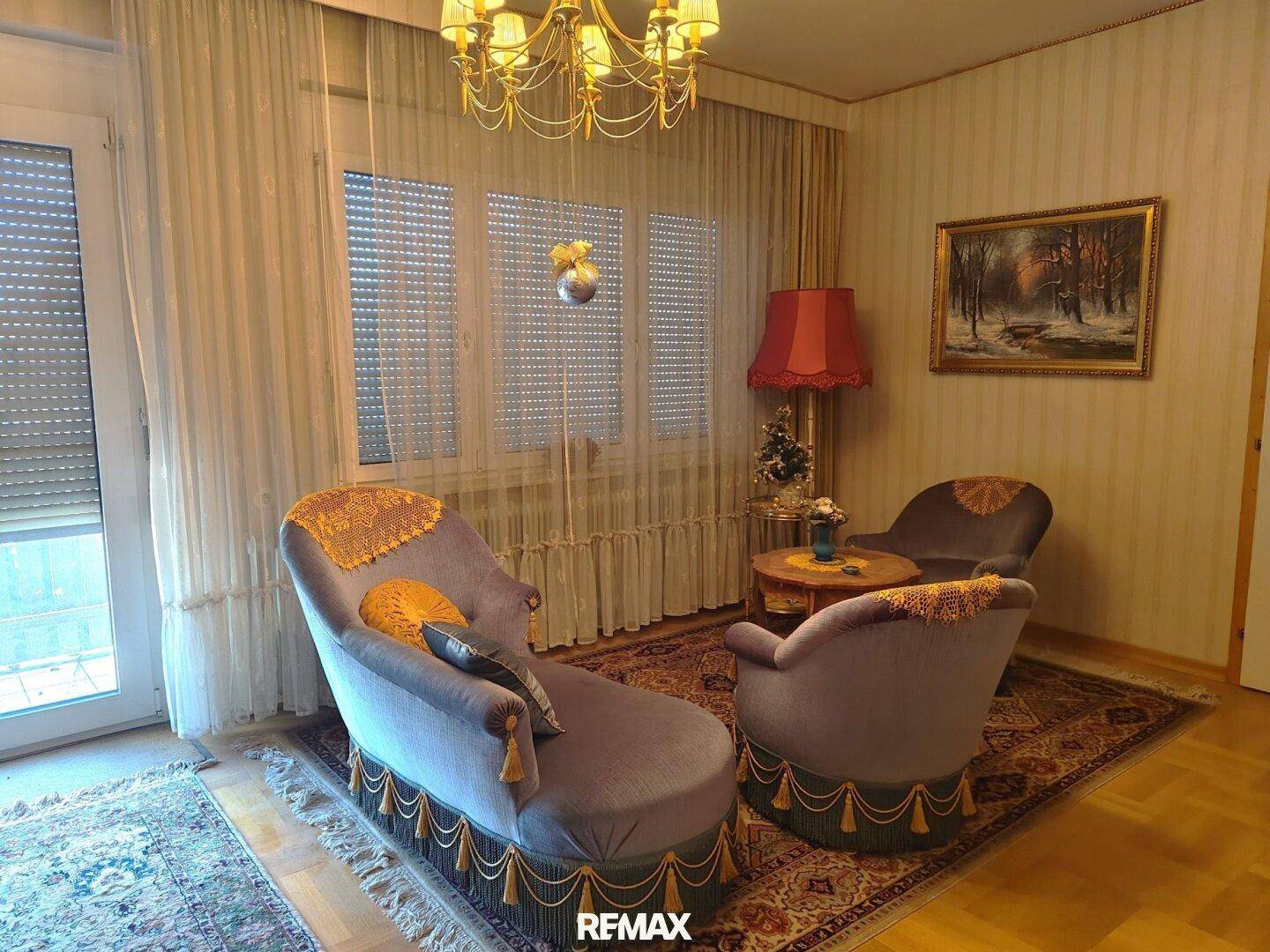 Wohnzimmer mit traditionellen Möbeln, Teppich und Zugang zu einem Balkon oder einer Terrasse.