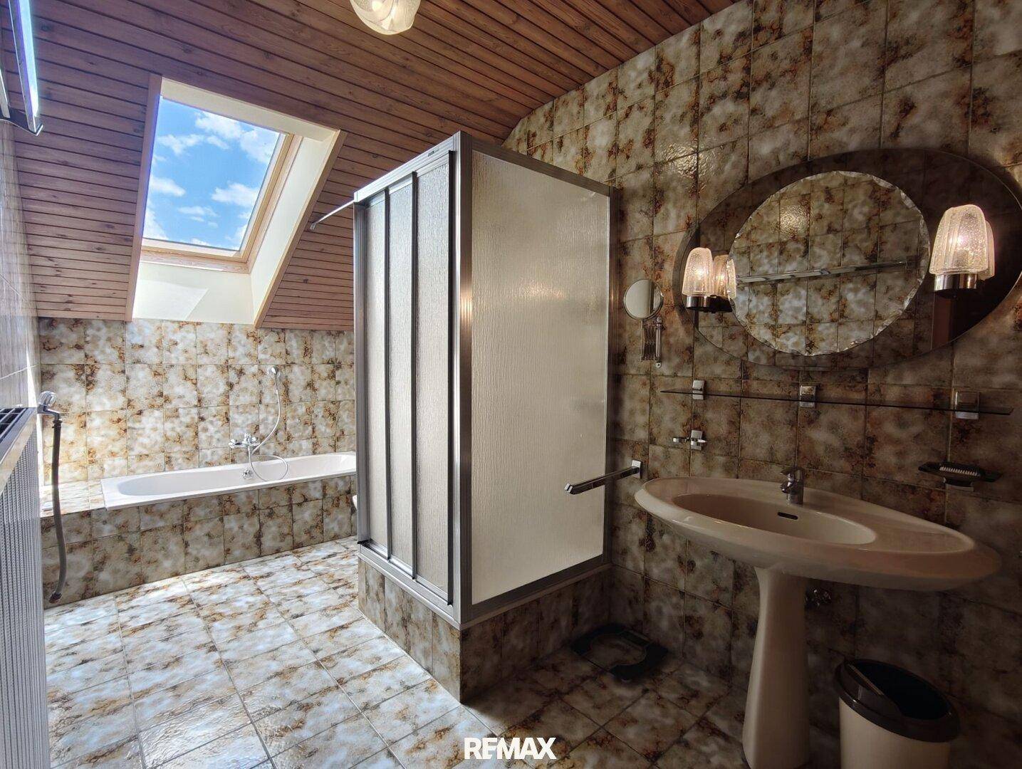 Dachgeschoss-Badezimmer mit Badewanne, Dusche, Waschbecken und Dachfenster.