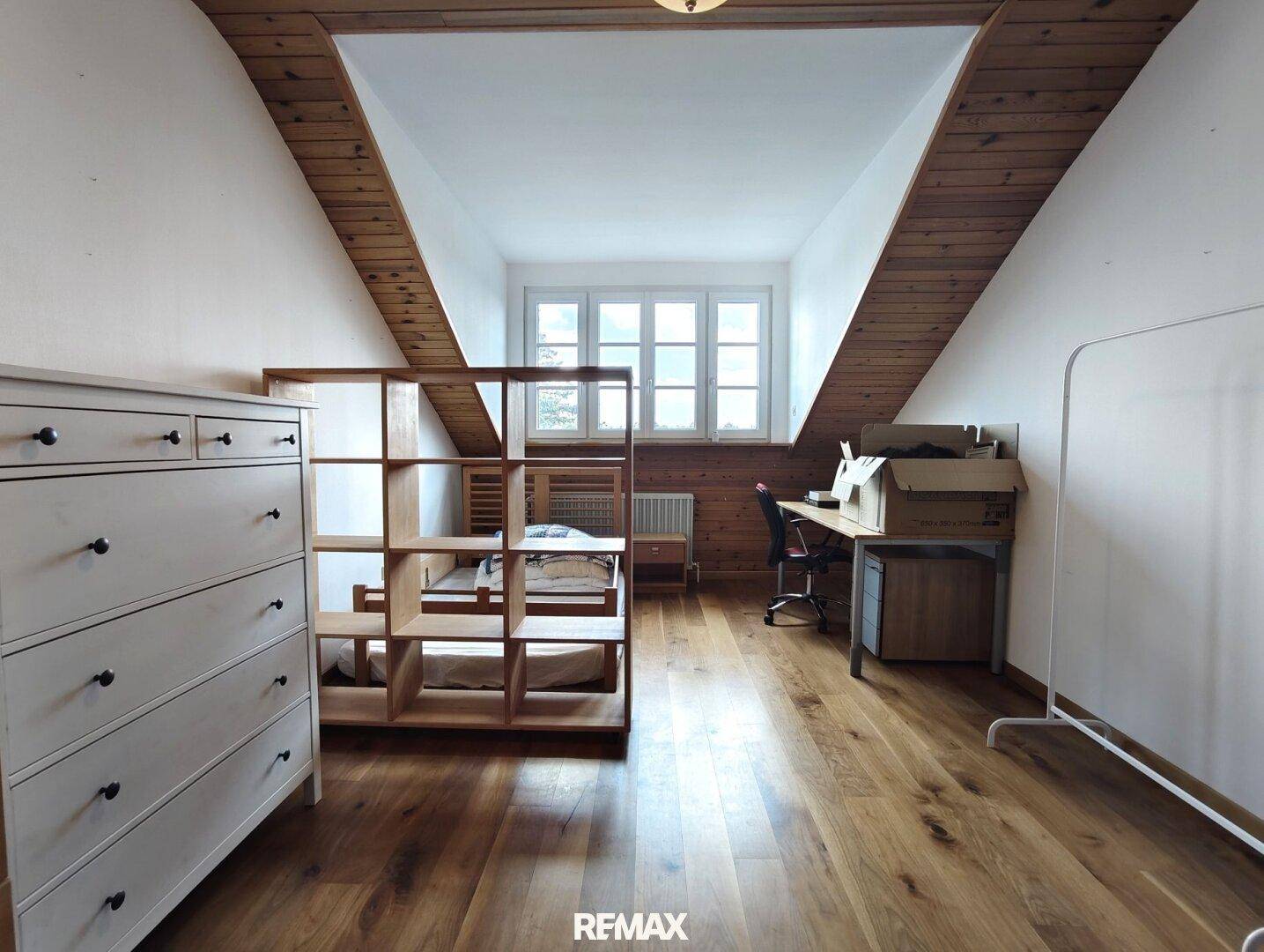 Dachgeschosszimmer mit Holzboden, Schreibtisch und Fenster, ideal als Büro oder Schlafzimmer.