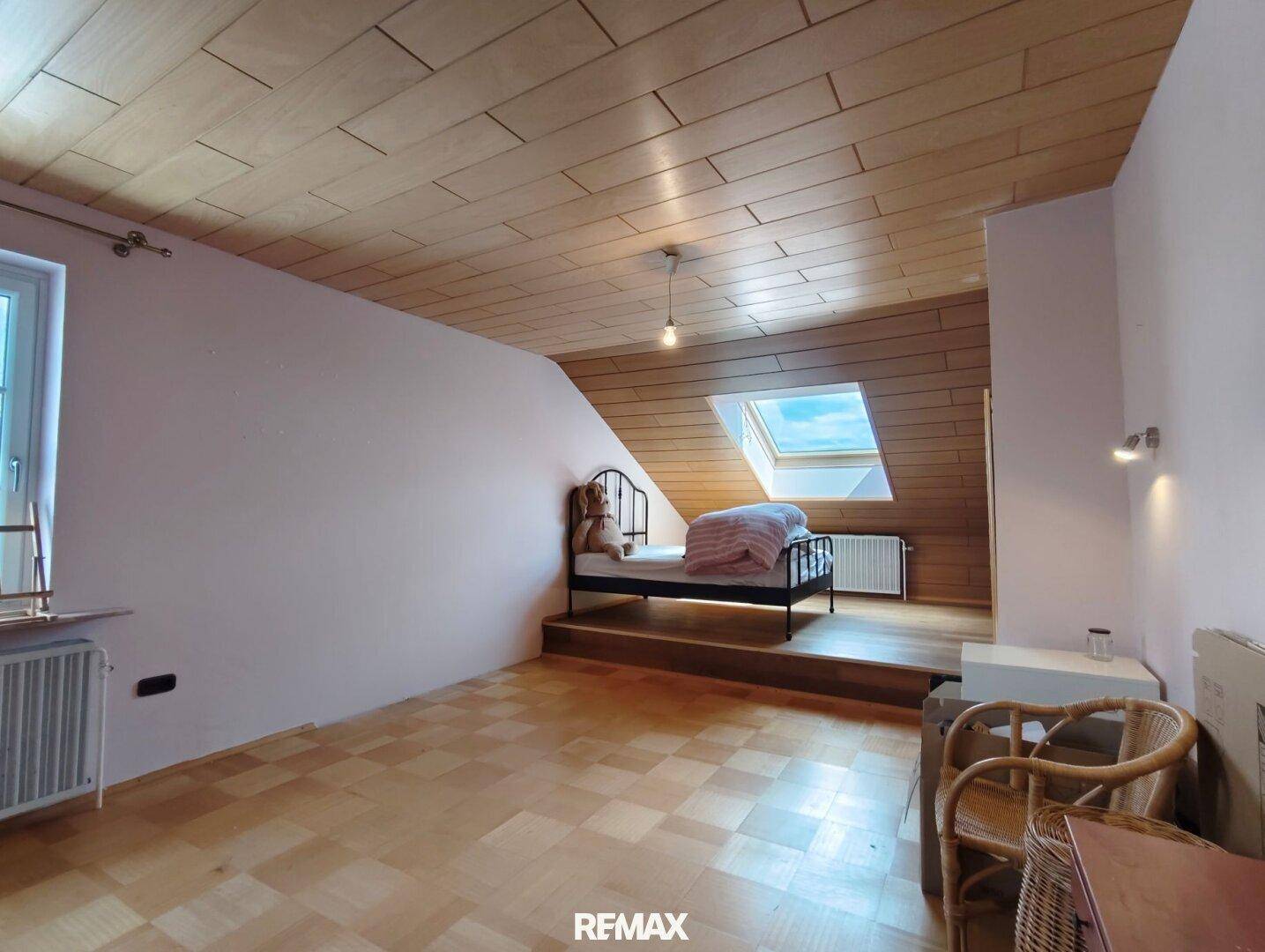 Helles Dachgeschoss-Schlafzimmer mit Holzboden, Dachfenster und rosa Wänden.