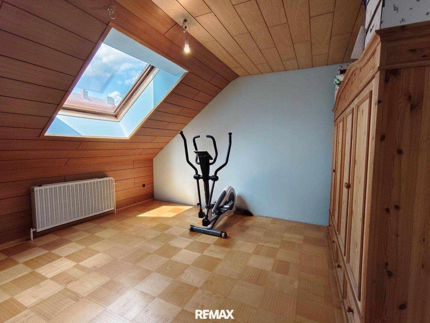 Dachgeschossraum mit Fitnessgerät, Holzboden und Dachfenster, ideal für Sport.
