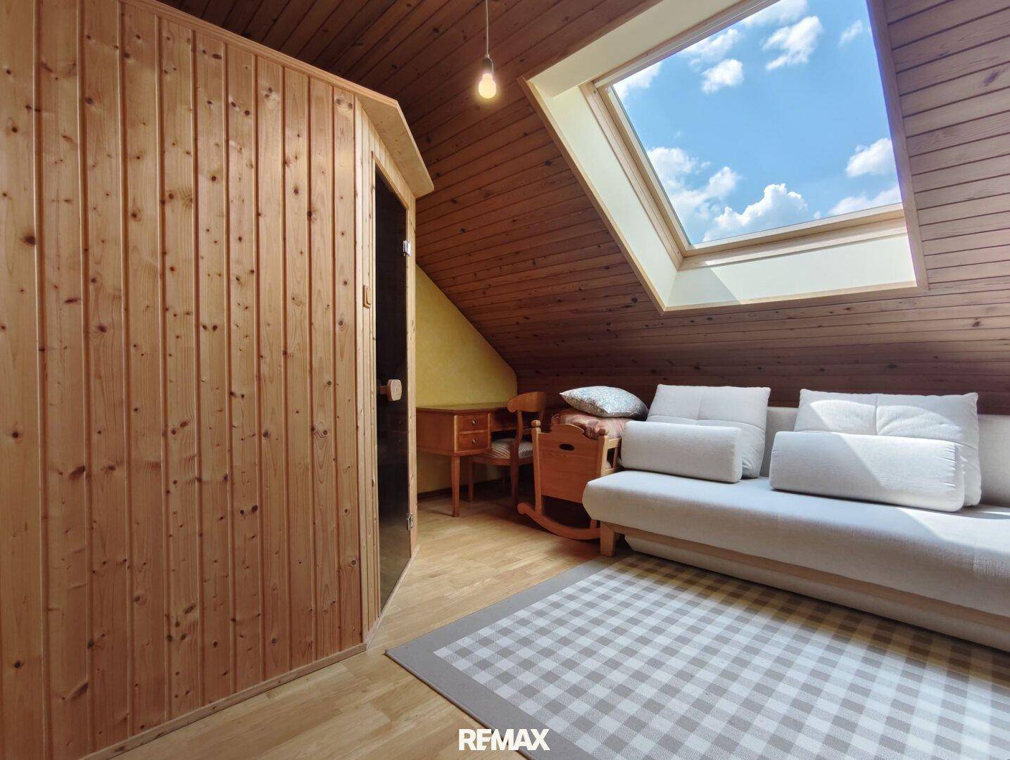 Dachgeschosszimmer mit Sauna, Dachfenster und gemütlicher Sitzecke unter der Holzdecke.