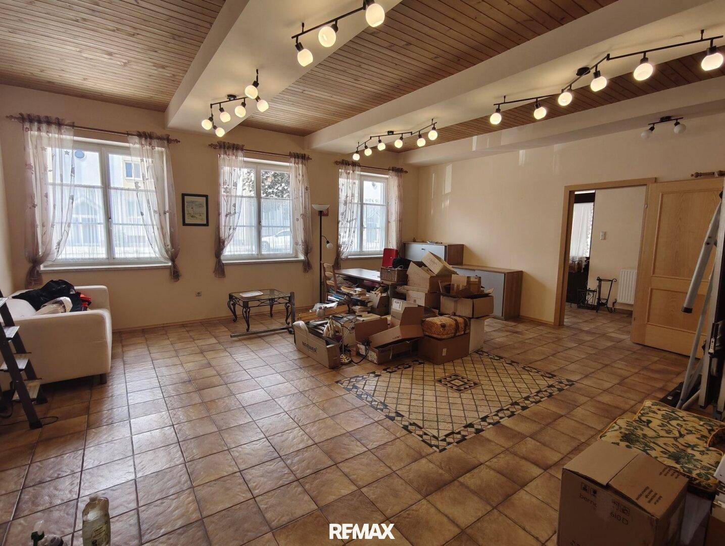 Großes, leeres Zimmer mit Holzbalkendecke, Fliesenboden und vielen Fenstern.