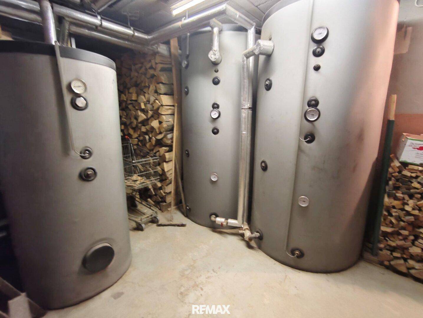 Lagerraum mit großen Warmwasserspeichern und gestapeltem Brennholz.